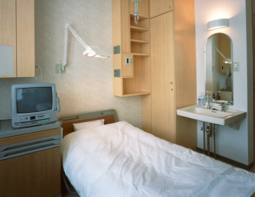 病棟個室の写真。シングルベッドに物置、テレビや洗面台が設置されている。